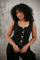 Woman wearing a black sleeveless top with gold buttons against a gray background