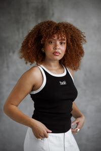 Person wearing a black tank top with white trim and text, standing against a gray background