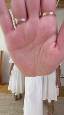 Woman's hand with rings, holding a white midi dress.
