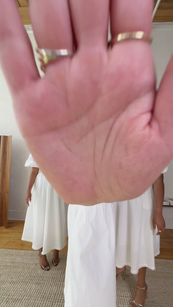 Woman's hand with rings, holding a white midi dress.